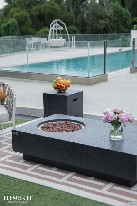 Outdoor setting with a Elementi fire pit, fruit bowl, and flowers by a pool.