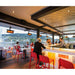 Modern outdoor bar with red chairs and people enjoying drinks by a waterfront.