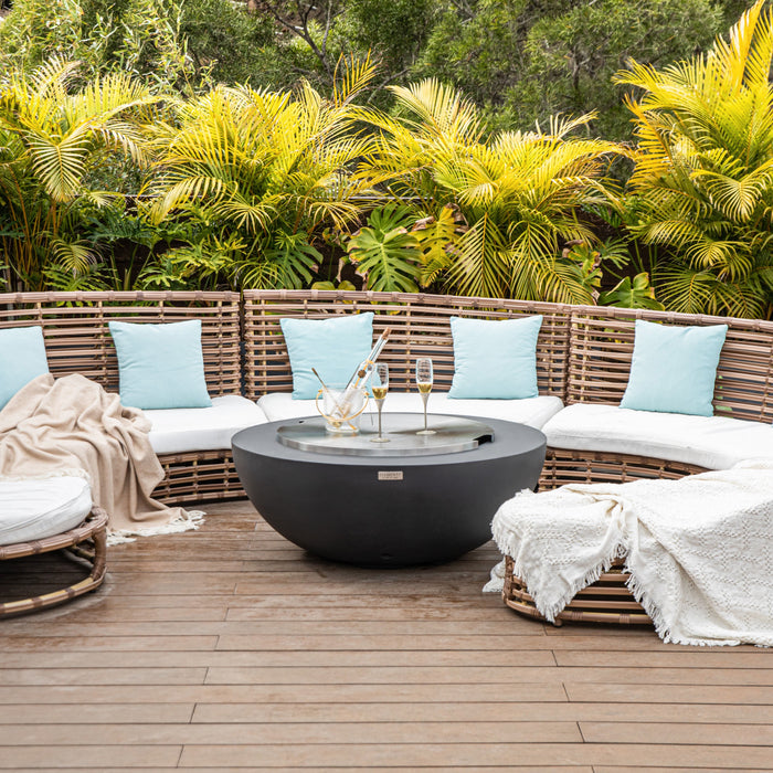 Outdoor seating area with wicker furniture, blue cushions, and the Elementi Lunar bowl fire pit table with the stainless steel lid in a tropical setting.