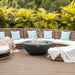Outdoor seating area with wicker furniture, blue cushions, and the Elementi Lunar bowl fire pit table with the stainless steel lid in a tropical setting.