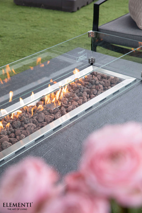 Elementi fire pit table with flames and a blurred floral arrangement in the foreground.