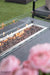 Elementi fire pit table with flames and a blurred floral arrangement in the foreground.