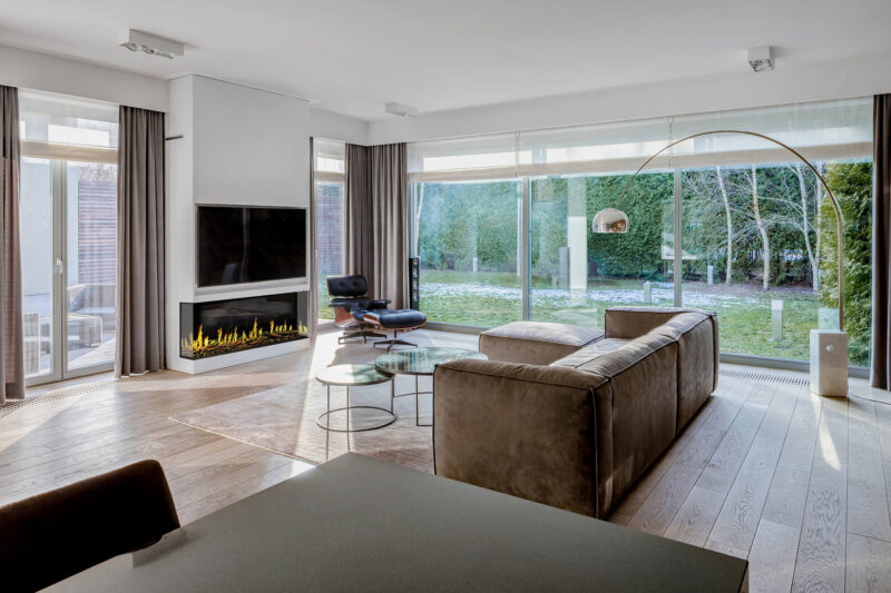 Modern living room with brown sofa, TV, and a 52 inch multi sided Orion Fireplace beneath the TV