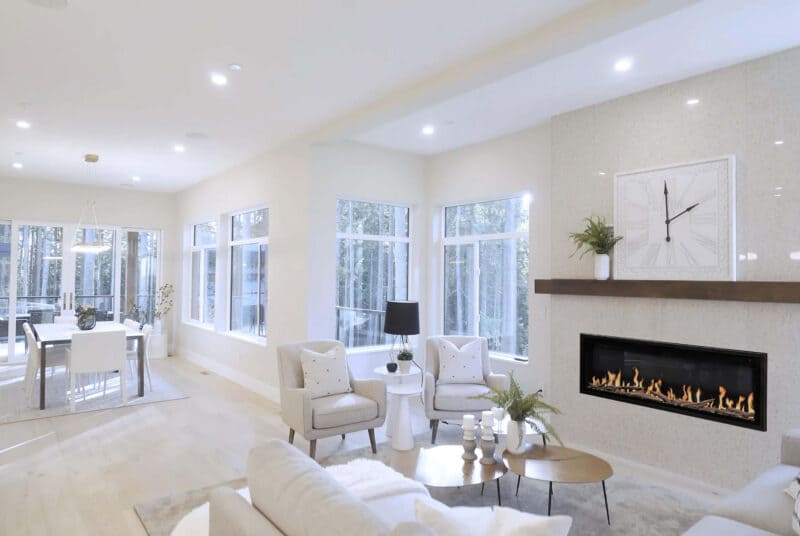 Modern living room with white furniture, fireplace, and large windows.