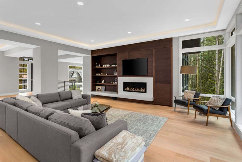 Modern living room with gray sofa, wooden floor, and large windows.