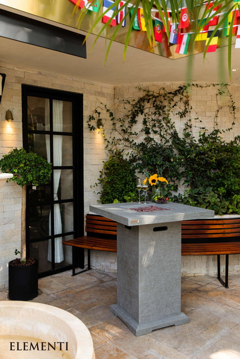 Outdoor patio area with an Elementi Montreal stone table, bench, and decorative flags.