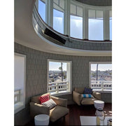 Modern living room with circular window design, a Bromic Platinum Electric Heater wall mounted above, and cityscape view