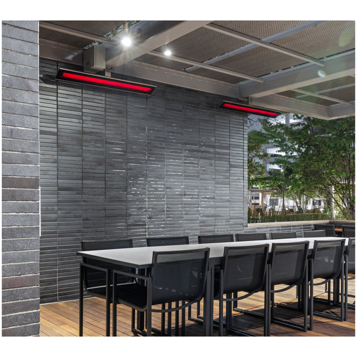 Outdoor seating area with tables and chairs under a ceiling mounted Platinum Heater by Bromic on a brick wall.