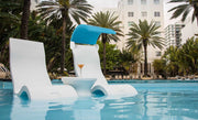 Hotel pool with two Ledge Lounger signature chairs and a side table in the middle and palm trees in the background