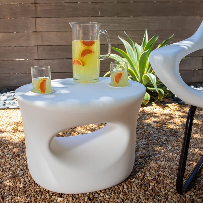 Outdoor setting with a white table holding a pitcher and glasses of lemonade with orange slices, next to a white chair.