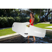 Woman in a red swimsuit carrying the  white TenJam Shayz Lounger by herself by the armrest hole in a pool, showcasing just how light the product is