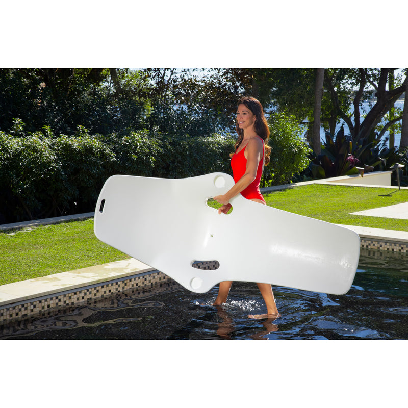 Woman in a red swimsuit carrying the  white TenJam Shayz Lounger by herself by the armrest hole in a pool, showcasing just how light the product is