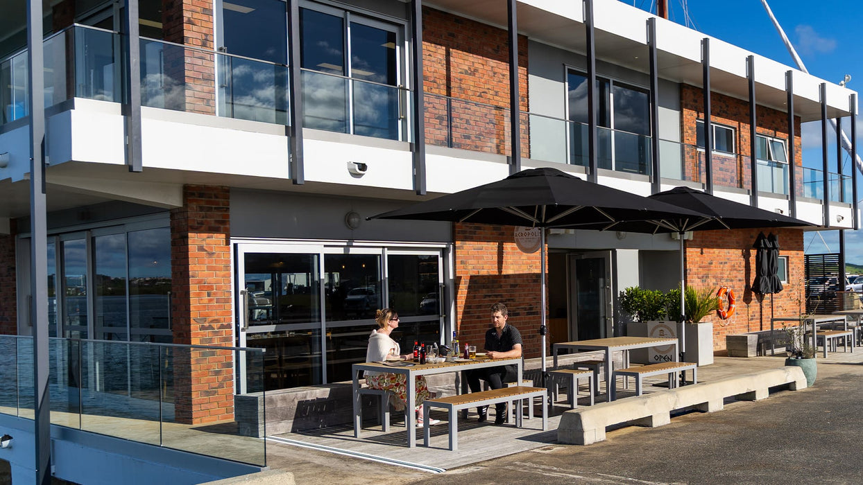 Modern building exterior with outdoor seating area covered by two Shadowspec Oasis Umbrellas
