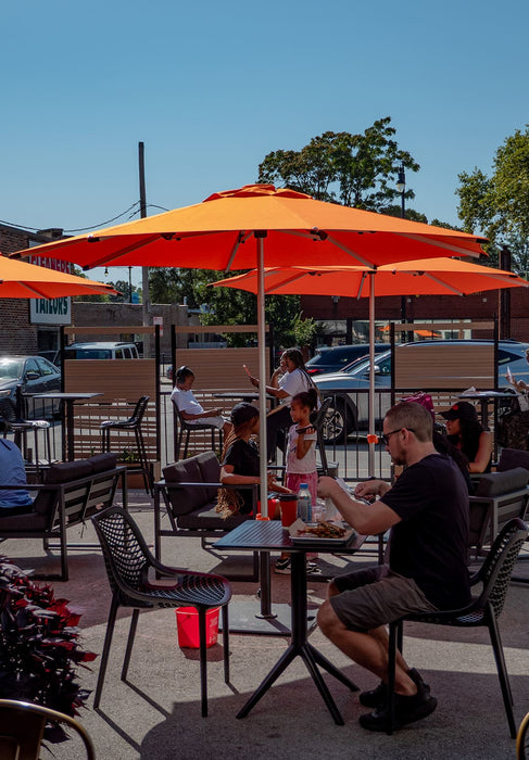 People dining outdoors under orange umbrellas on a sunny day.