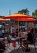 People dining outdoors under orange umbrellas on a sunny day.