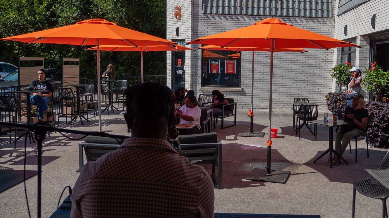 People sitting under orange umbrellas in an outdoor seating area.