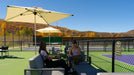 Two women sitting on a patio in front of a tennis court at a country club with umbrellas and a scenic background