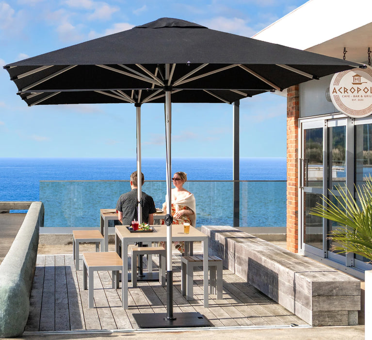 Two people sitting under a large black umbrella by Shadowspec on a rooftop with ocean view