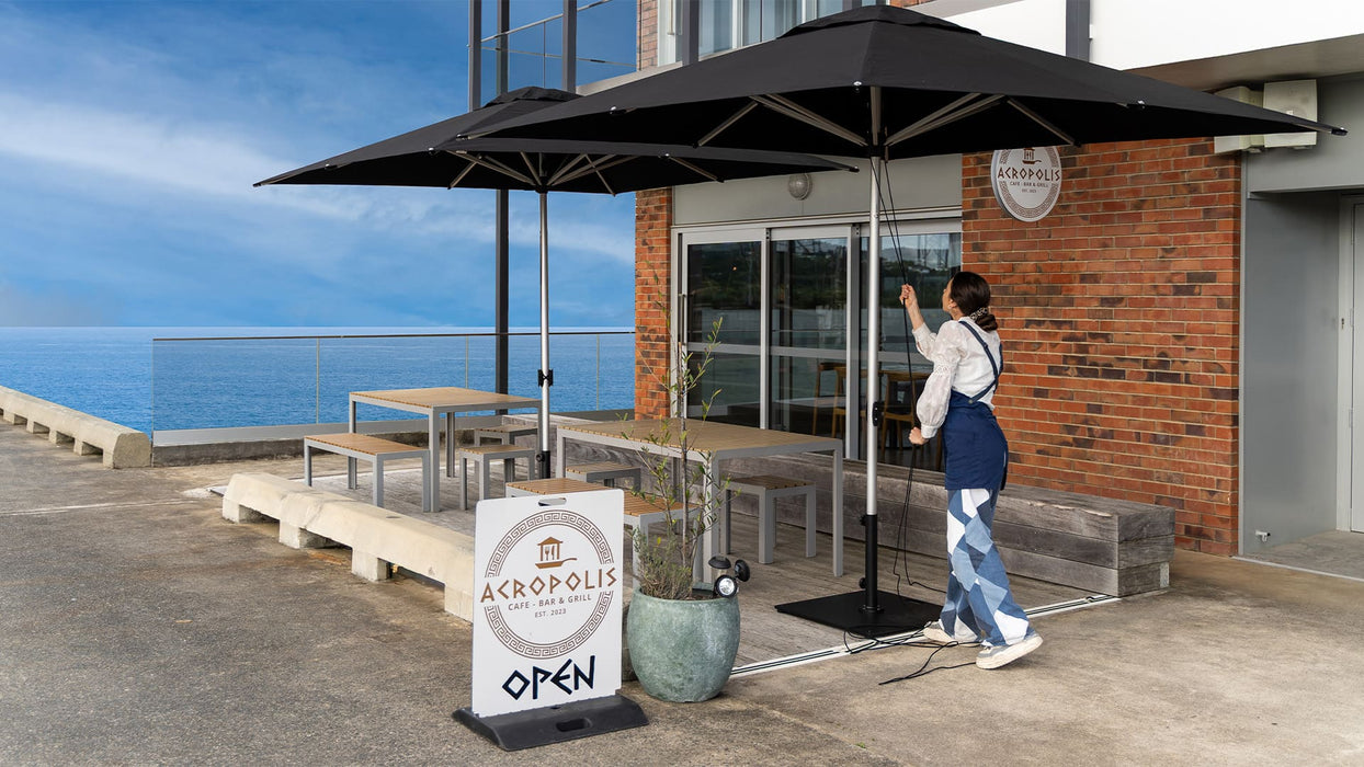 Person opening a large black outdoor  Shadowspec umbrella on a patio with ocean view