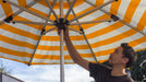 Person operating a large yellow and white striped umbrella outdoors