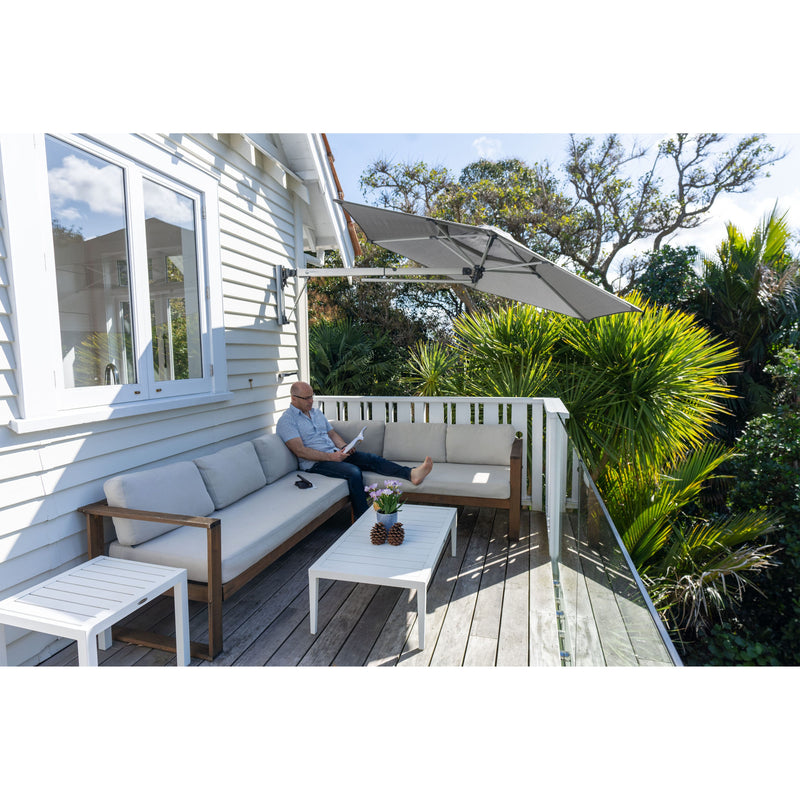Man sitting on patio reading a book under the shade provided by the Shadowspec Retreat wall mounted umbrella