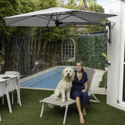 Woman with a dog sitting on a lounge chair under a Shadowspec Retreat umbrella by a pool.