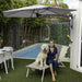 Woman with a dog sitting on a lounge chair under a Shadowspec Retreat umbrella by a pool.