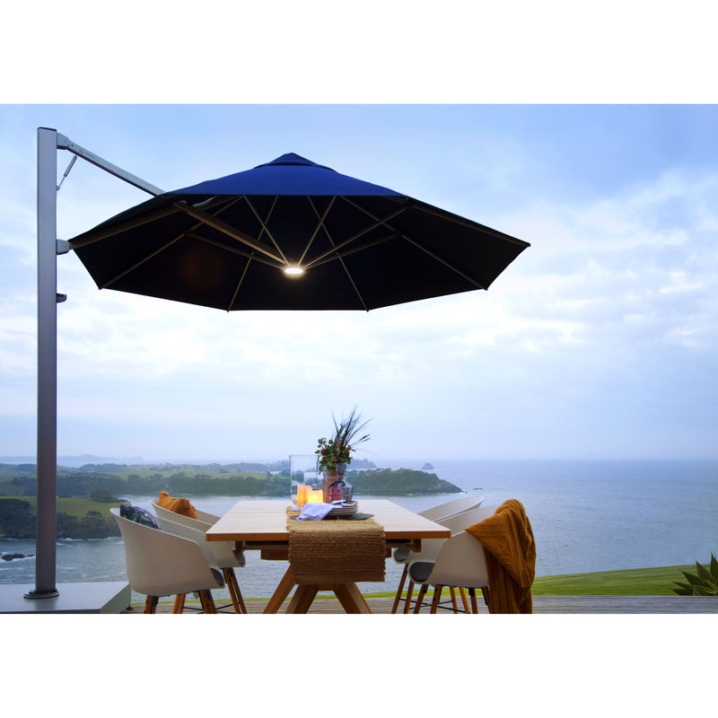 Shadowspec Serenity cantilever umbrella with LED light over a dinner table in front of an ocean view