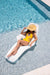 Woman in yellow swimsuit and hat lounging on a white inflatable pool float in clear blue water.