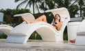 Woman lounging on a modern white Deep signature chaise with palm trees in the background