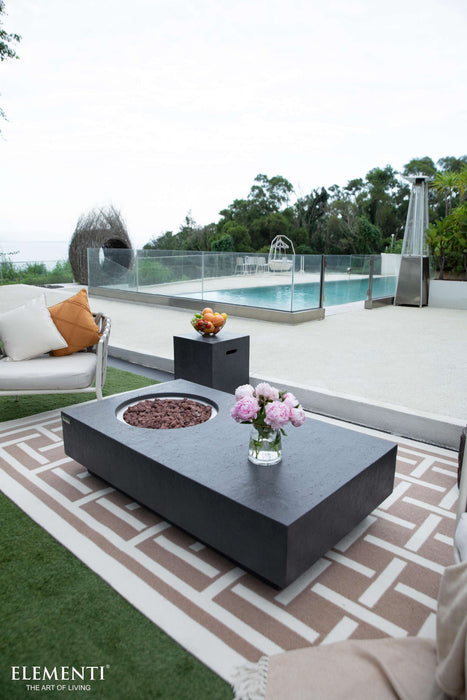 Outdoor patio with Elementi Metropolis Fire table, chairs, and pool in the background