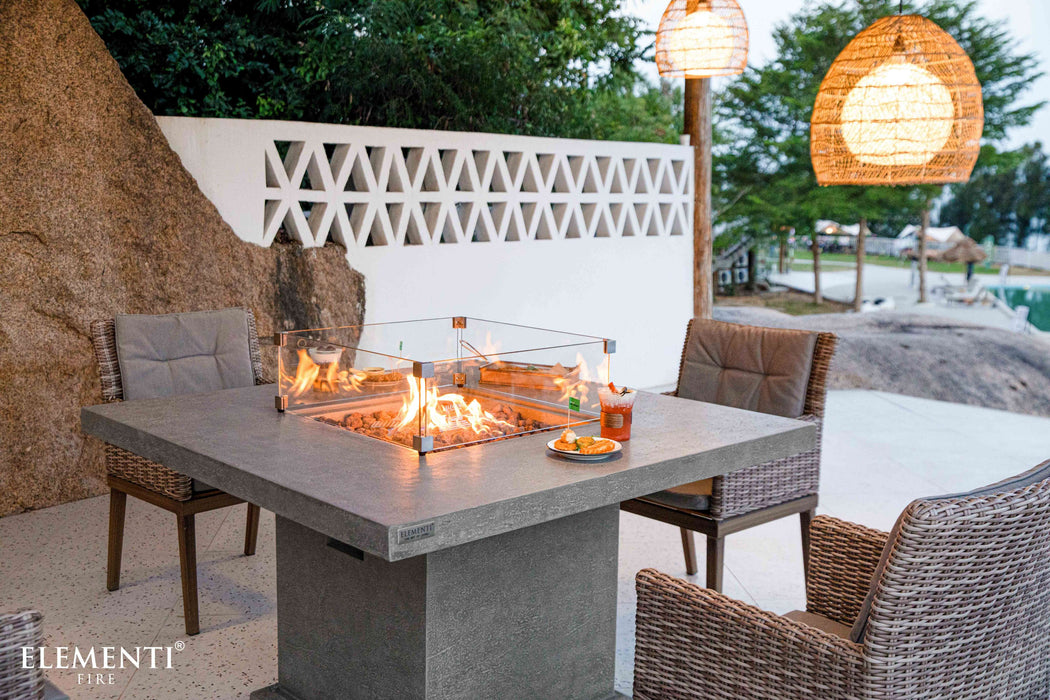 Outdoor patio setting with Elementi fire pit table, chairs, and pool in the background