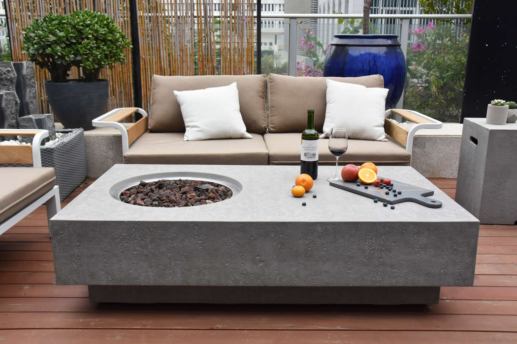 Outdoor patio setting with a Elementi Metropolis fire pit table, sofa, and decorative items.