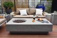 Outdoor patio setting with a Elementi Metropolis fire pit table, sofa, and decorative items.