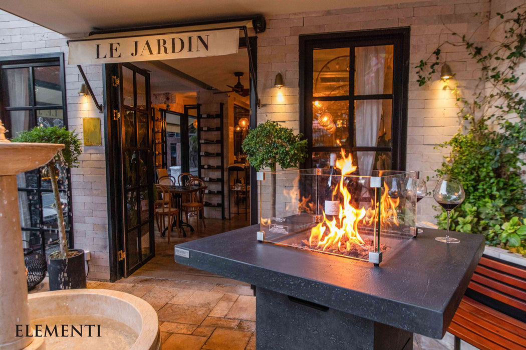 Outdoor patio with Elementi Montreal fire pit, plants, and 'Le Jardin' restaurant entrance.