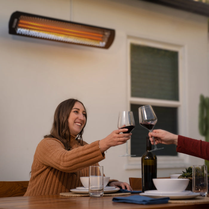 Two people toasting with wine glasses at a table with a Bromic heater above.
