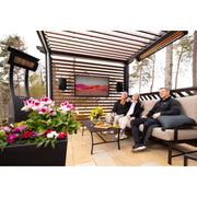 People sitting on a patio with a TV screen, outdoor speakers, and decorative plants. Modern Bromic Patio Heaters displayed in setting as well