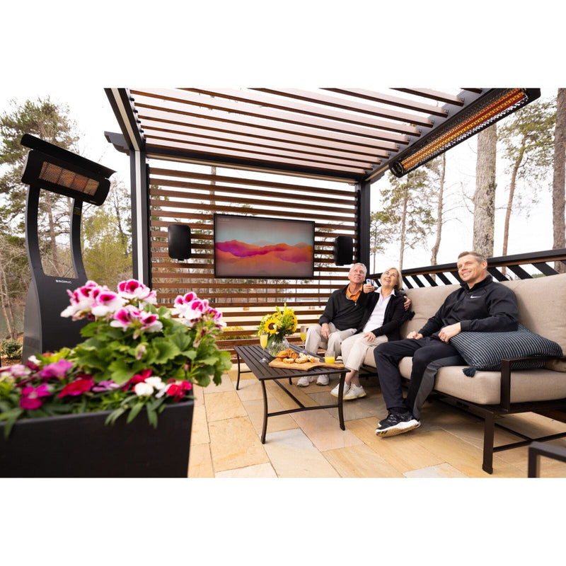 People sitting on a patio with a TV screen, outdoor speakers, and decorative plants. Modern Bromic Patio Heaters displayed in setting as well