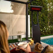 Person holding a mug by a pool with a freestanding outdoor heater in the background