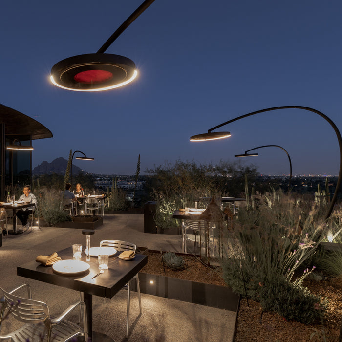 Outdoor dining area at night with tables, chairs, and people seated under modern Bromic Eclipse Portable heaters that appear like luxurious streetlights.