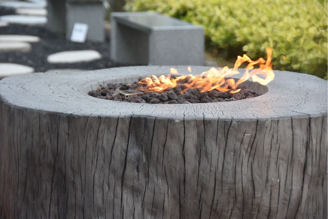 Elementi Manchester Fire pit made from a tree stump with flames burning inside, surrounded by greenery.