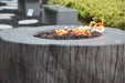 Elementi Manchester Fire pit made from a tree stump with flames burning inside, surrounded by greenery.