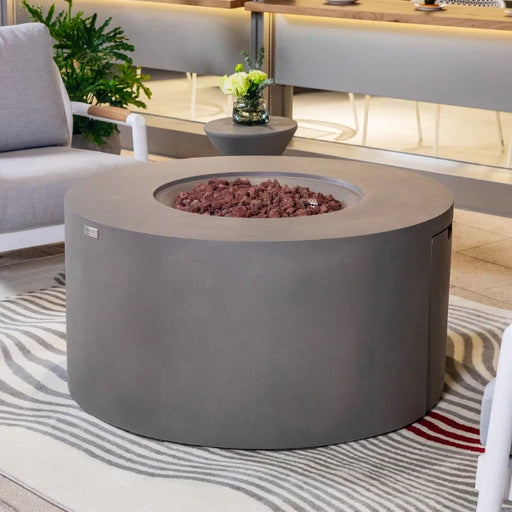 Round concrete fire pit table in a modern living room setting with gray sofa and striped rug.