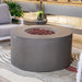 Round concrete fire pit table in a modern living room setting with gray sofa and striped rug.