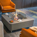 Modern living room with a Gray elementi fire pit table, orange chairs, and gray sofa.