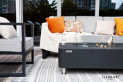 Outdoor patio setting with a fire pit table, gray sofa, and colorful cushions.
