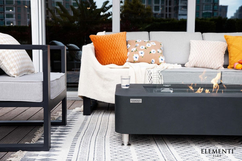 Outdoor patio setting with a fire pit table, gray sofa, and colorful cushions.