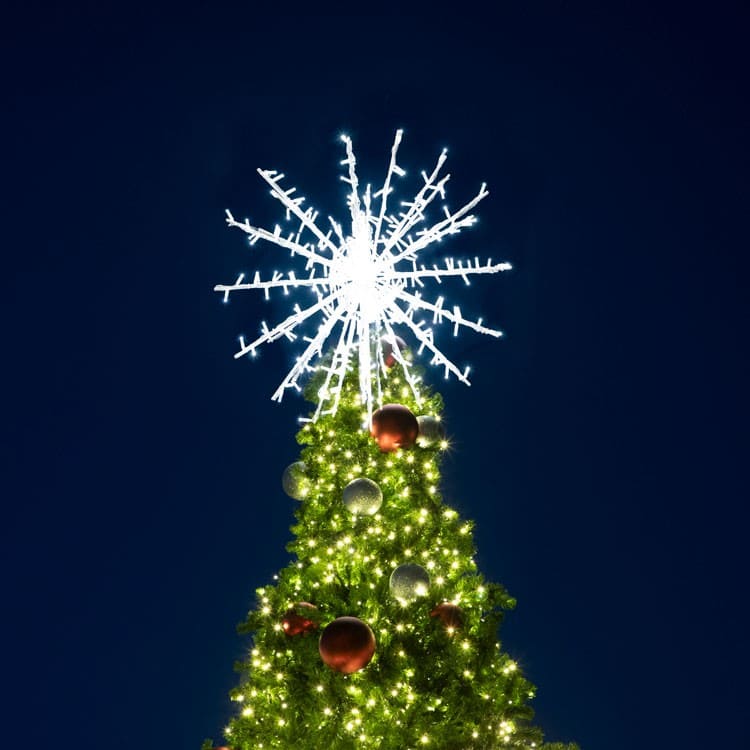 Decorated Christmas tree with a large snowflake light on a dark blue sky background