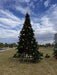 Decorated Christmas tree with colorful ornaments on a grassy area under a blue sky with clouds.