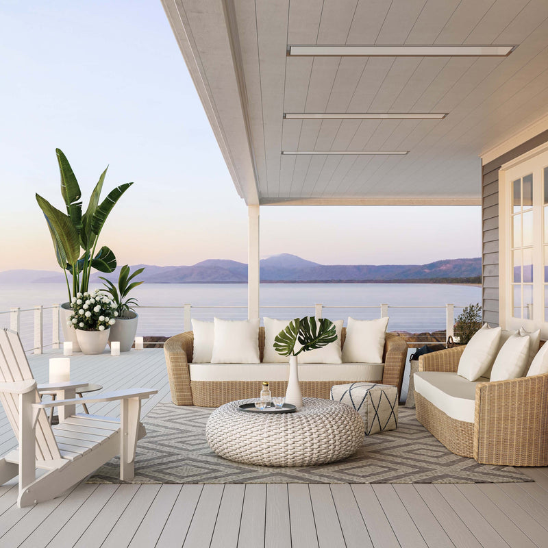Outdoor patio with wicker furniture, cushions, and a scenic view of mountains and water. White Bromic Marine Heaters pictured flush mounted into the ceiling above